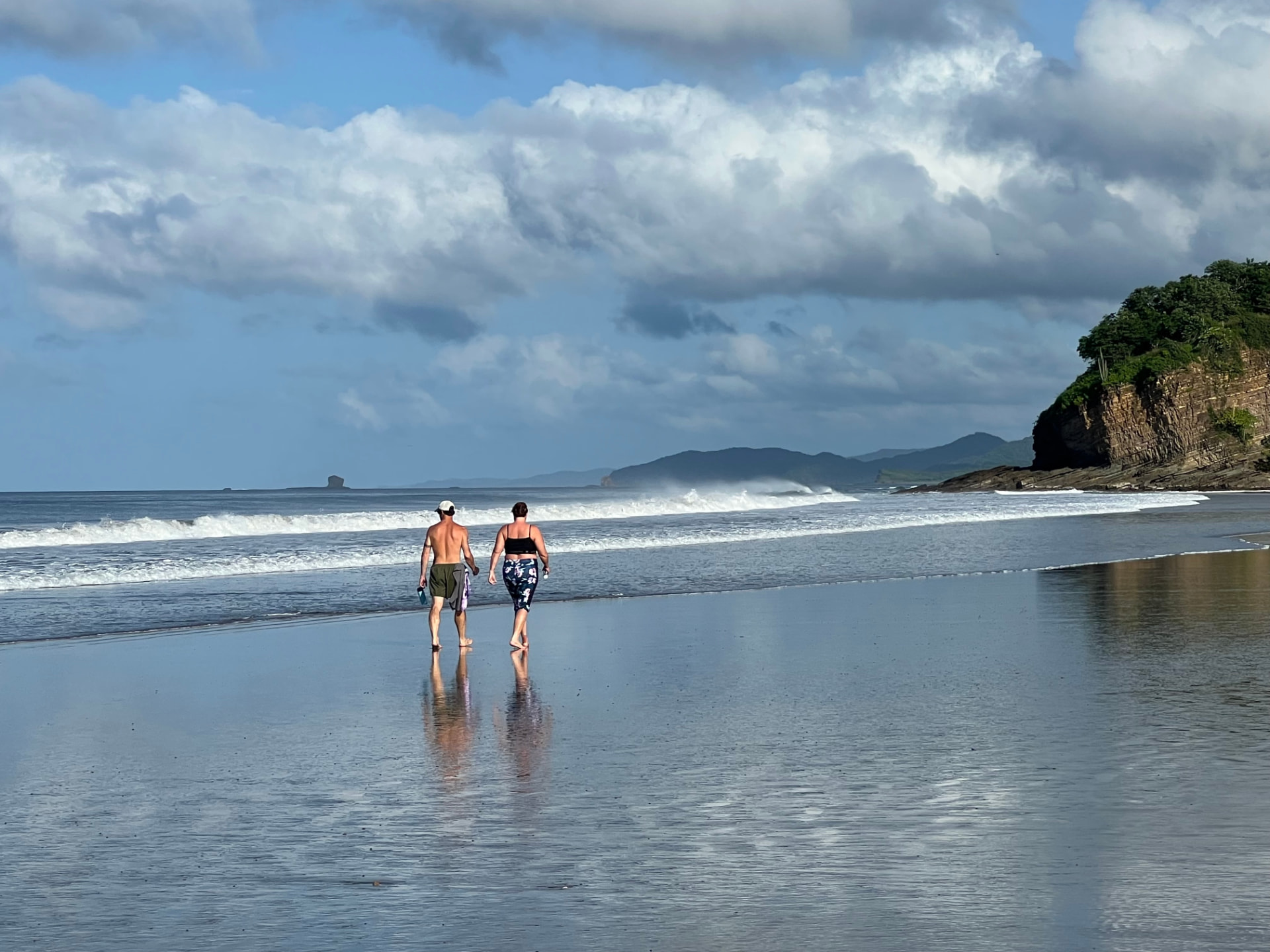 A couple walking together across the reflective shoreline at Playa El Coco