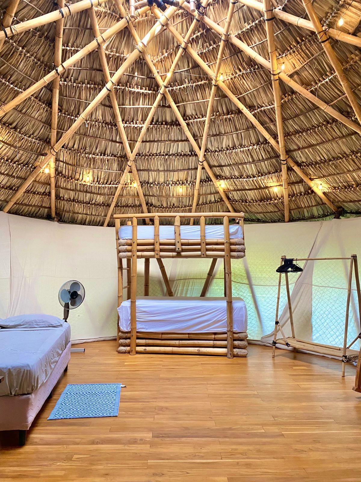 A room with a wooden bed frame, bright bedding and windows opening onto tropical greenery