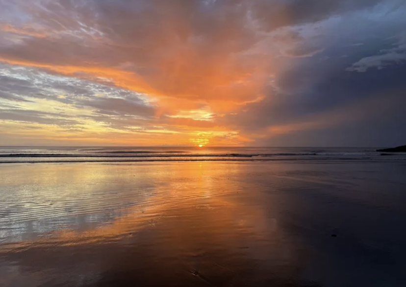 Orange sunset over a reflective beach with dark clouds over the ocean