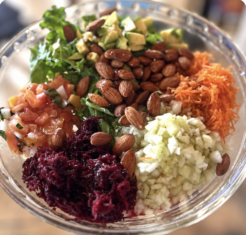 A colorful bowl of fresh vegetables, greens, avocado and almonds