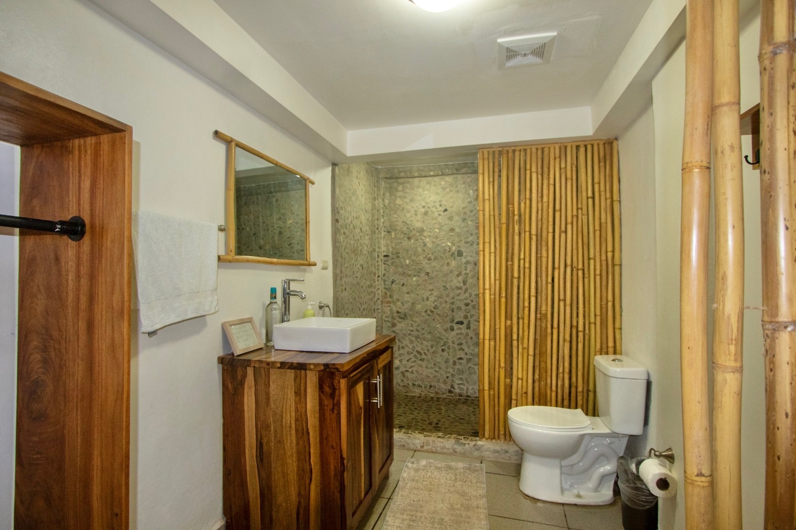 A bathroom with a live-edge wooden vanity, bamboo screen and a stone-pebble shower