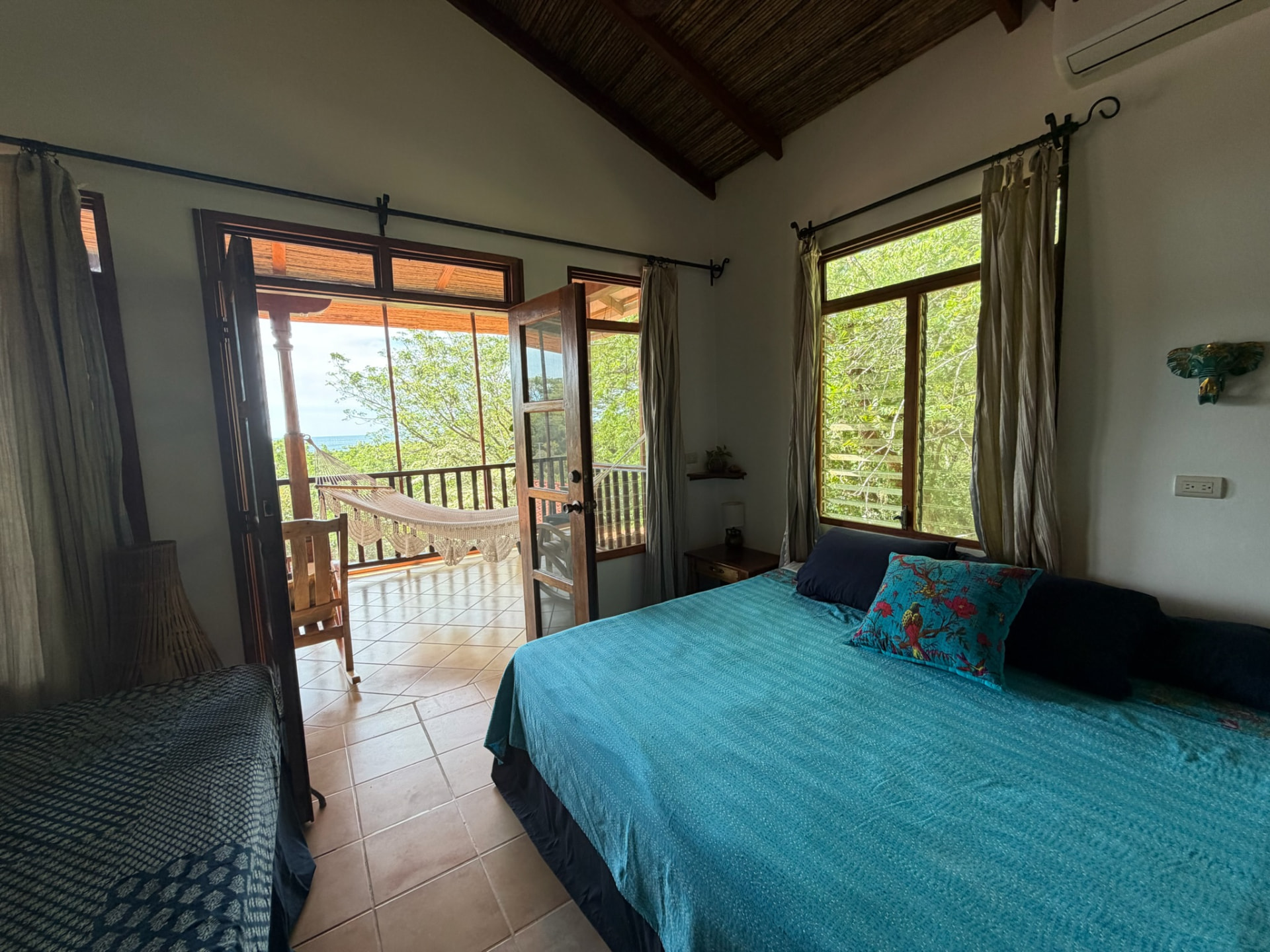 A room with two beds and doors open onto a balcony with a hammock and view toward the ocean