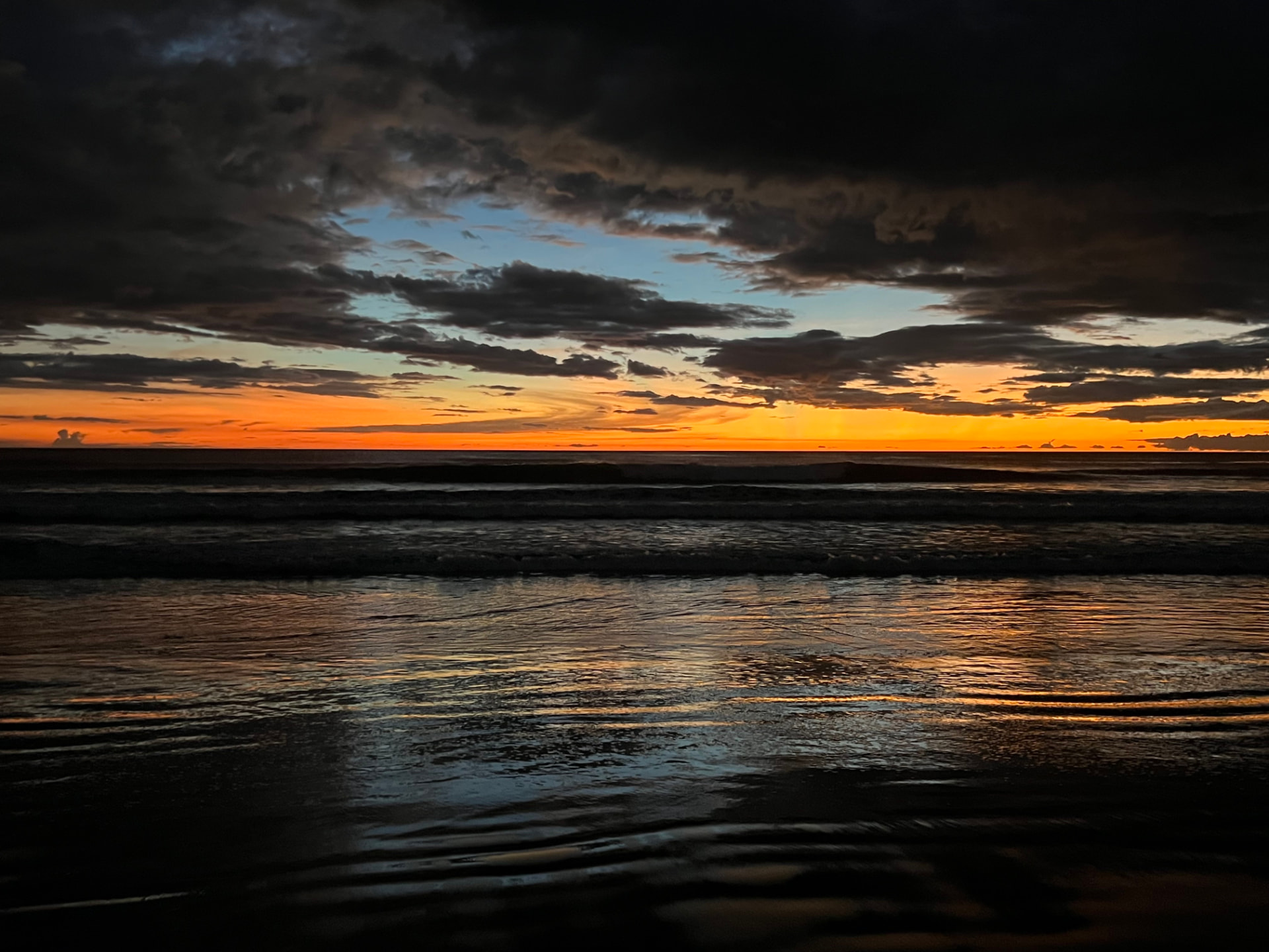A vivid orange sunset beneath dramatic clouds over the Pacific
