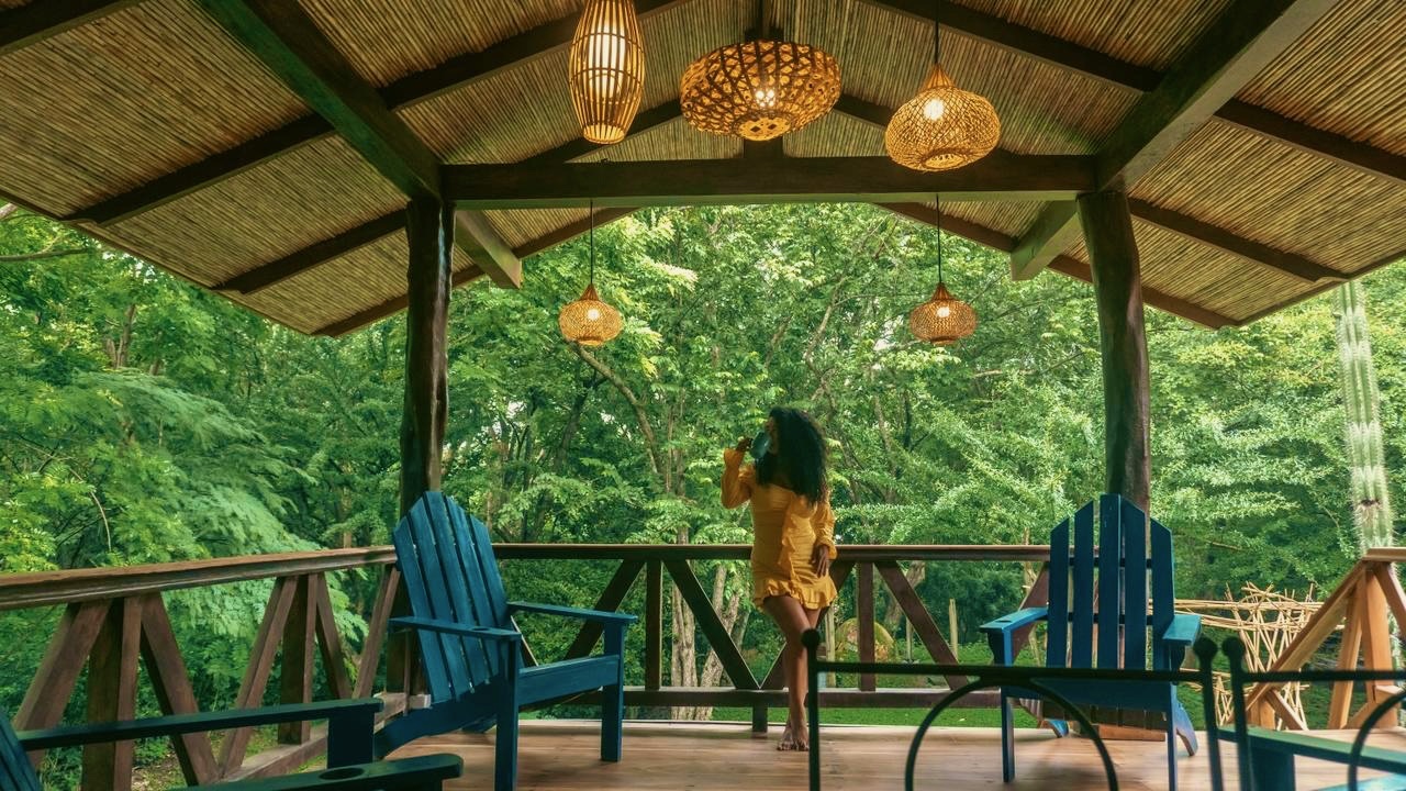 A person pausing with a drink on an open-air terrace surrounded by jungle