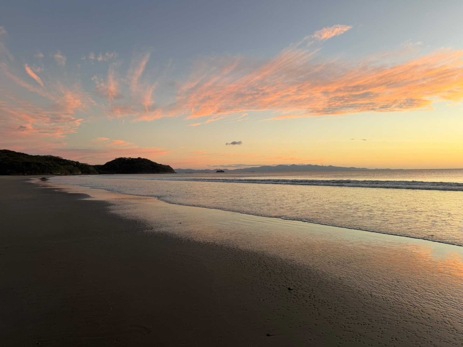 Soft pink and gold light over the bay, headland and wet sand at dawn