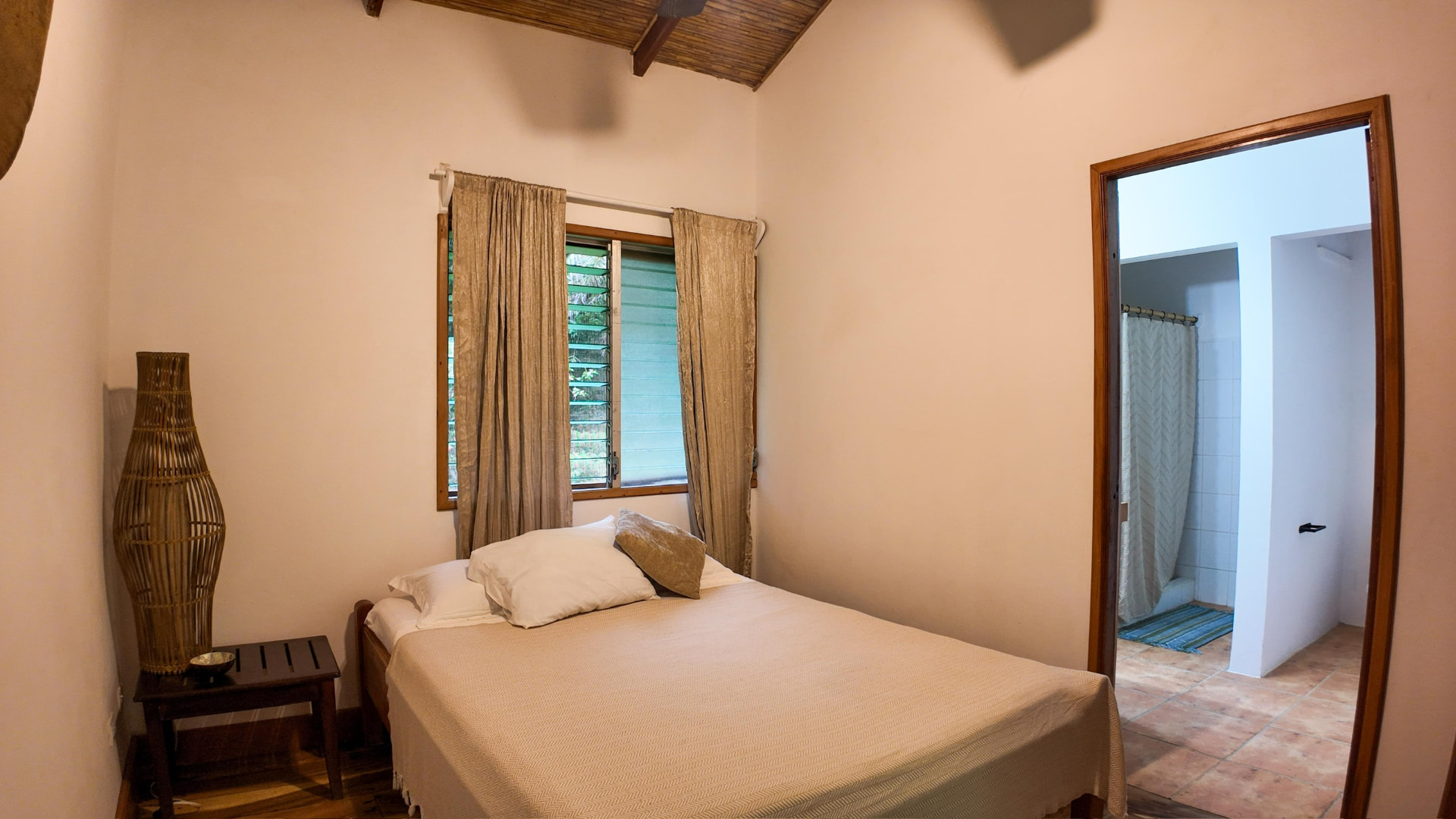 A simple room with a double bed, bamboo ceiling and adjoining bathroom