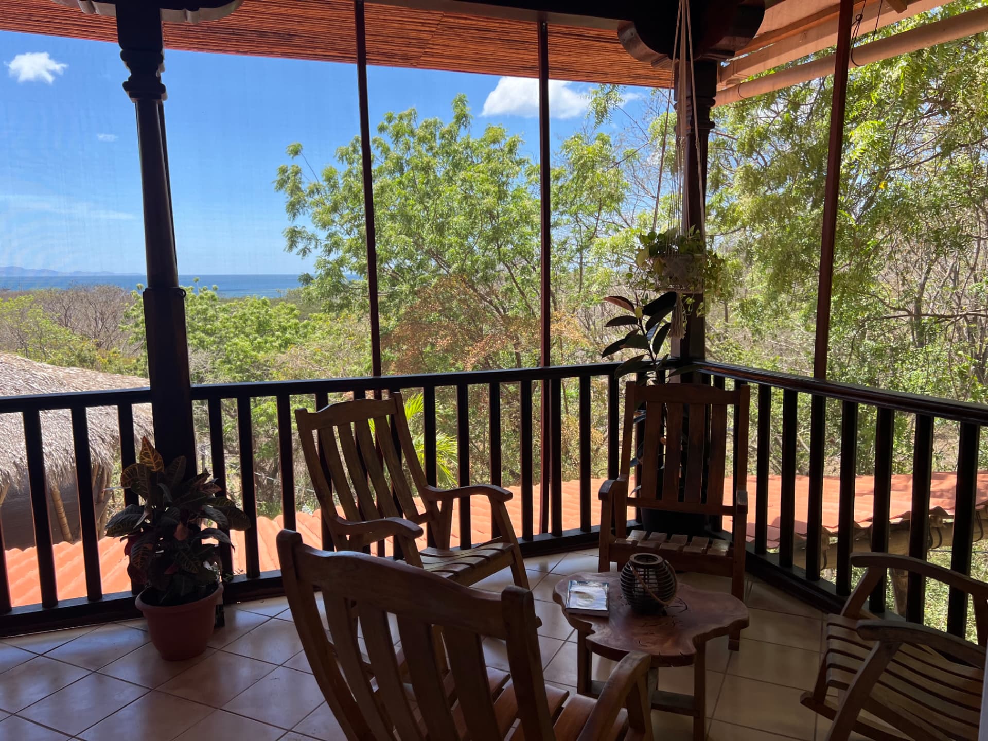 Wooden rocking chairs on a screened porch overlooking treetops and the ocean beyond
