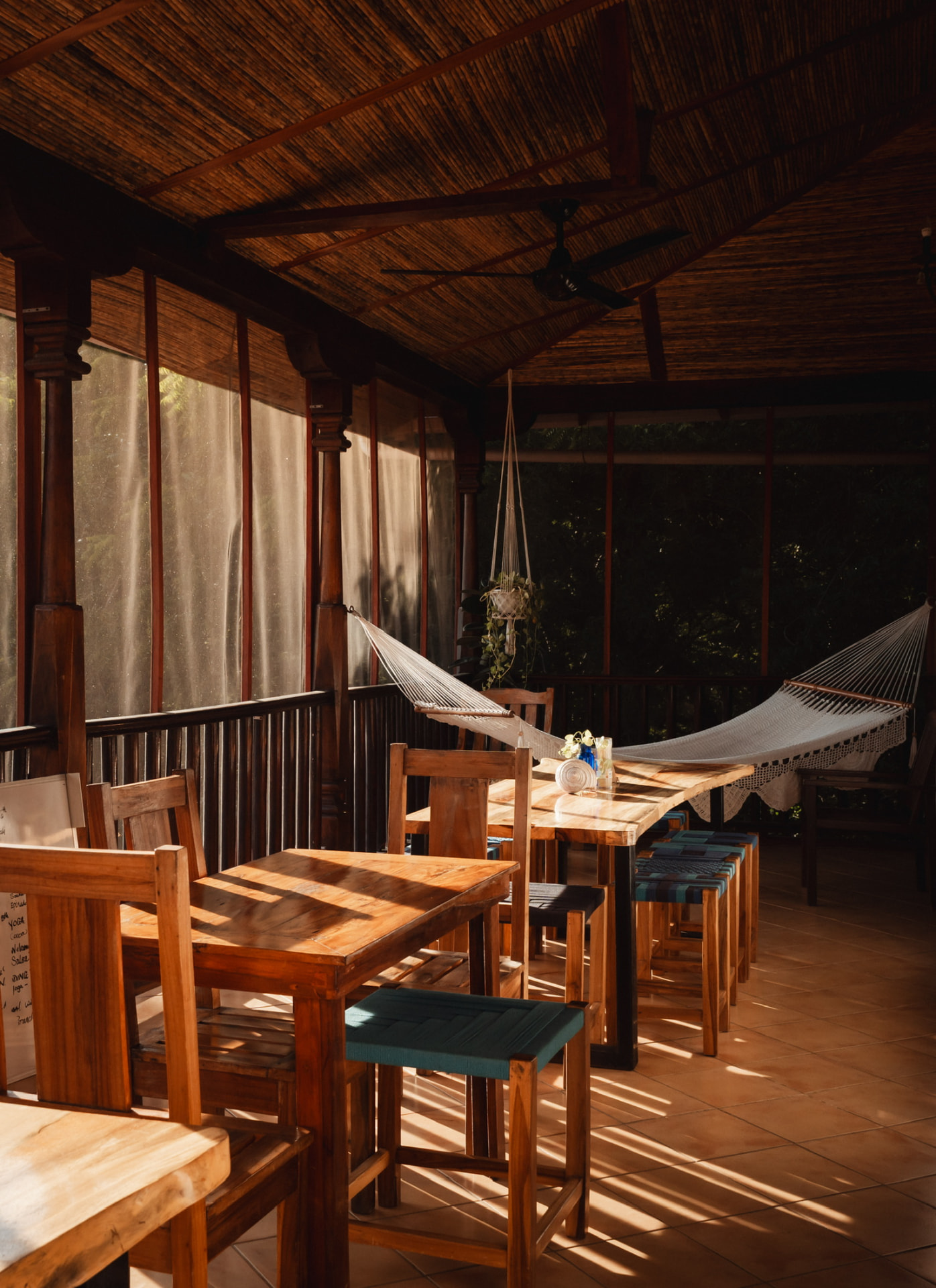 A hammock and chairs on a shaded terrace with afternoon shadows across the floor