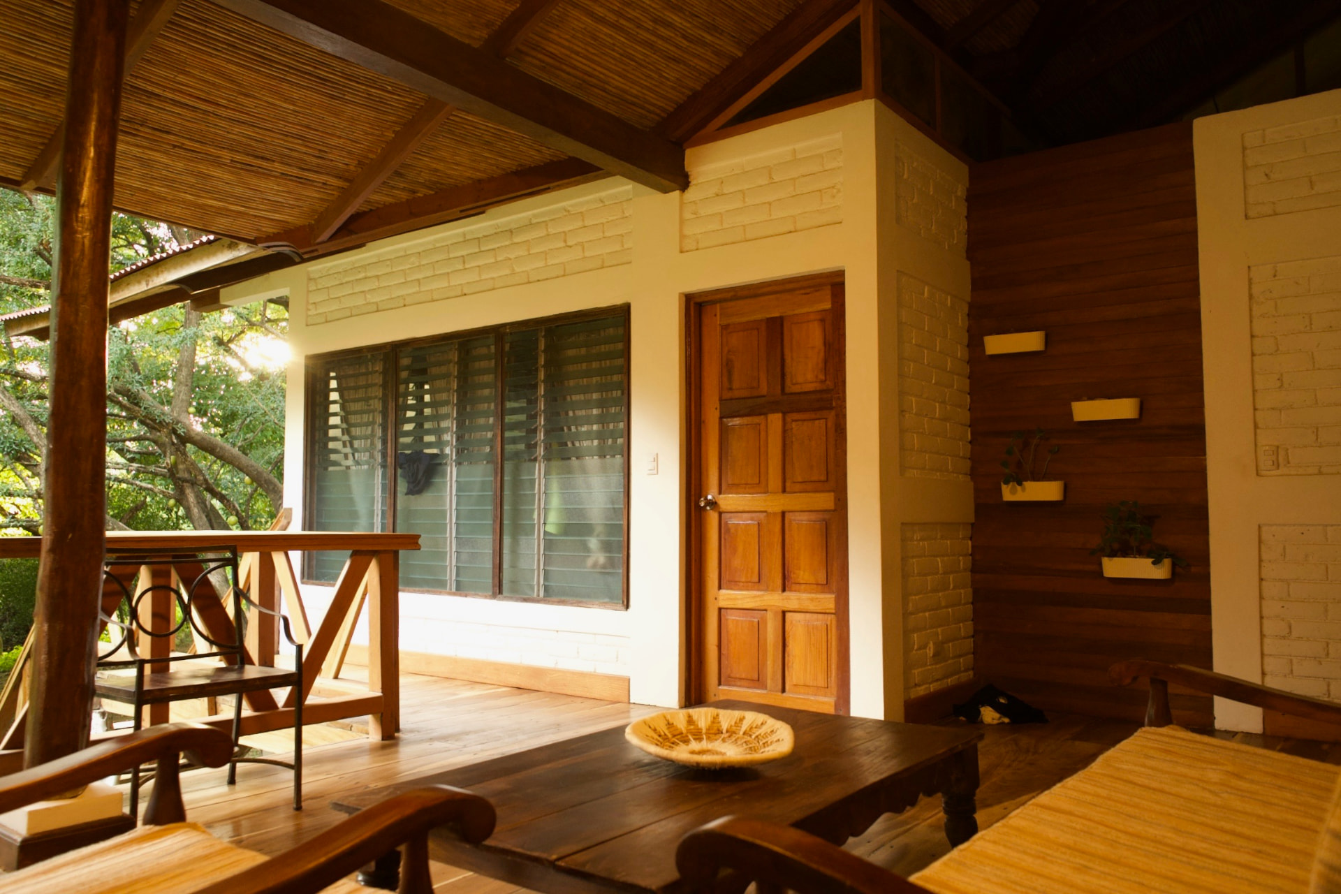 A covered wooden walkway with seating outside a guest room door in warm afternoon light