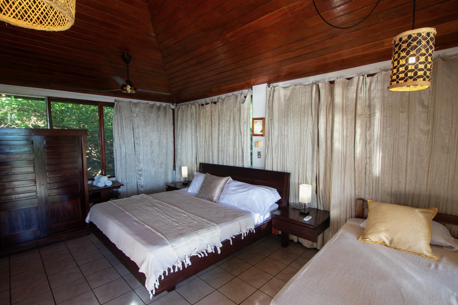 A room with a double and a single bed, wood-panelled ceiling and forest views